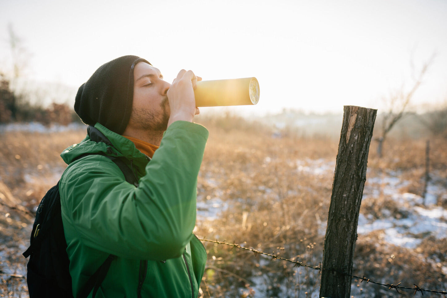 Man, in een besneeuwd bosgebied drinkend uit een thermosfles